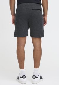 Dunkelgraue Sportshorts aus strukturiertem Stoff, mit einer Reißverschlusstasche auf der Rückseite und einem elastischen Bund. Kombiniert mit weißen Sneakers.