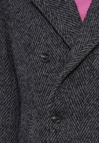 Hall halli kala luudriidega vöökang, millel on tekstuurse koega muster, kahel mustal nupul ja sügava sälkluuga kraega. Taustavärv on roosa.