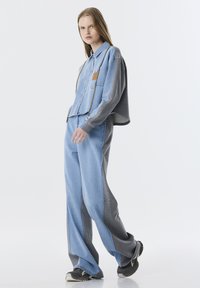 Denim blouse en broek set met een grijs en lichtblauw kleurenschema, voorzien van een cropped ontwerp, zakaccenten en textuurdetails in de stof.