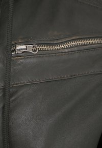 Schwarzes Ledergewebe mit einem sichtbaren Reißverschluss. Ausführliche Nähte entlang der Nähte und ein glänzender metallischer Reißverschluss an der Tasche für sicheren Verschluss.