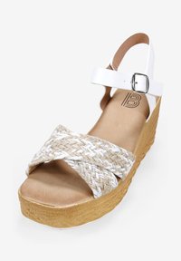 Sandalia de cuña con una correa trenzada de aspecto yute en beige y blanco, una correa ajustable en blanco para el tobillo y una suela de plataforma texturizada en beige.