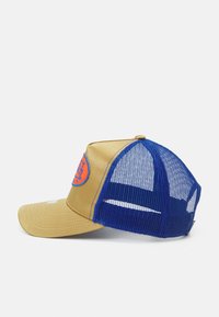 Gorra trucker color canela con una parte frontal estructurada, paneles de malla azules, visera curvada y un logo circular naranja en el panel frontal.