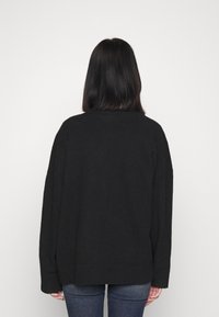 Svart oversized tröja med texturerad yta, ribbade ärmslut och nederkant, designad med en avslappnad passform, sedd bakifrån.