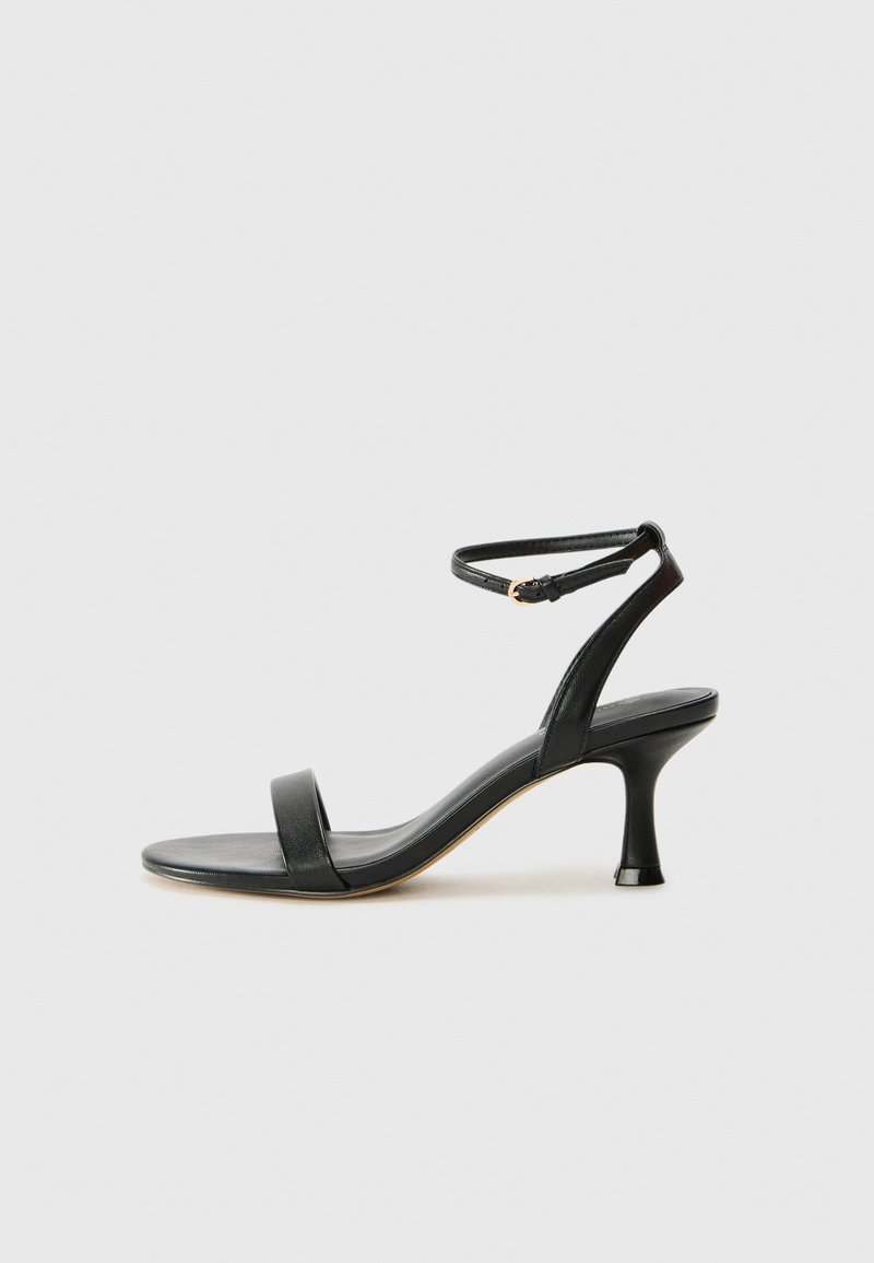 Sandale à talon en cuir noir avec une sangle de cheville, présentant un design élégant, un bout ouvert et un talon effilé pour une silhouette épurée.