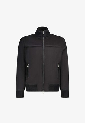 Giacca nera con zip frontale, colletto alto a costine, tasche laterali con zip e polsini a costine. Presenta una texture del tessuto liscia e un design minimalista.