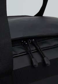 Bolsa aislante negra con superficie brillante, tela gruesa, cierre de doble cremallera y correas negras duraderas para facilitar el transporte.