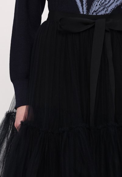Black tulle skirt with layered ruffles, featuring a cinched waist and a satin ribbon belt. Textured fabric creates a voluminous appearance.