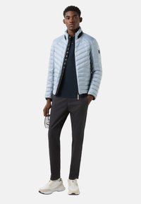 Jasnoniebieska pikowana kurtka o dopasowanym fasonie, granatowy kołnierz i zapięcie na suwak. Nosi się ją na granatową koszulkę polo, w połączeniu z ciemnymi spodniami i sneakersami.