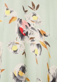 Ljusgrön tyg med texturerad yta som har ett abstrakt blommönster i vita, svarta, gula, orange, rosa och röda nyanser.