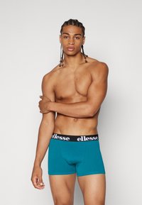 Türkise Baumwollboxershorts mit einem schwarzen Bund, der das "ellesse"-Logo in Weiß trägt. Glatte Textur und enganliegendes Design, ideal für den täglichen Gebrauch.