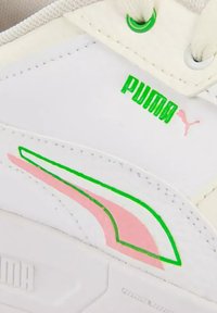 Section de basket Puma blanche avec logo Puma vert et rose et détails de design près des lacets blancs et des panneaux cousus.