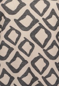 Beiger Stoff mit großen, unregelmäßigen, dunkelgrauen Rauten. Das Design zeigt ein weiches, strukturiertes Baumwollmaterial.
