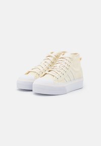 Höga sneakers i ljusbeige kanvas med vita gummisulor, med en texturerad yta och flera öglor för snören.