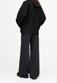 Sort oversized jakke med sænkede skuldre, kombineret med vidde mørkegrå bukser. Stoffet virker blødt med en mat finish.