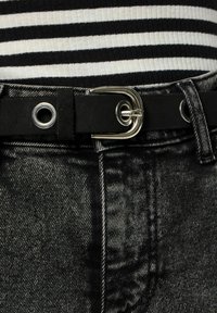 Vaqueros de denim negro con una superficie texturizada, que cuentan con un cinturón negro con una hebilla plateada y ojales. Blusa a rayas en blanco y negro.
