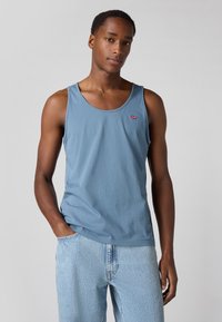 Un débardeur en coton bleu clair avec un col rond et un petit logo rouge sur la poitrine, associé à un jean en denim clair.
