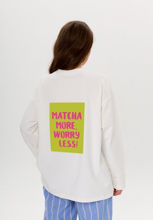Weißer übergroßer Hoodie mit einem grünen grafischen Rechteck auf dem Rücken, das pinken Text zeigt: "MATCHA MEHR, SORGE WENIGER!"