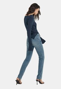 Top a maniche lunghe navy con scollo rotondo, abbinato a jeans skinny azzurri e tacchi aperti neri, mostrato in vista laterale.
