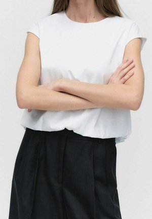 Hvid croptop med korte ærmer, glat tekstur og afslappet pasform, kombineret med sorte bukser med høj talje.