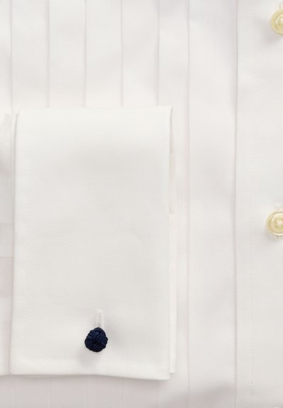 Primo piano di un polsino di camicia bianca con un gemello nodo blu navy attaccato all'asola.