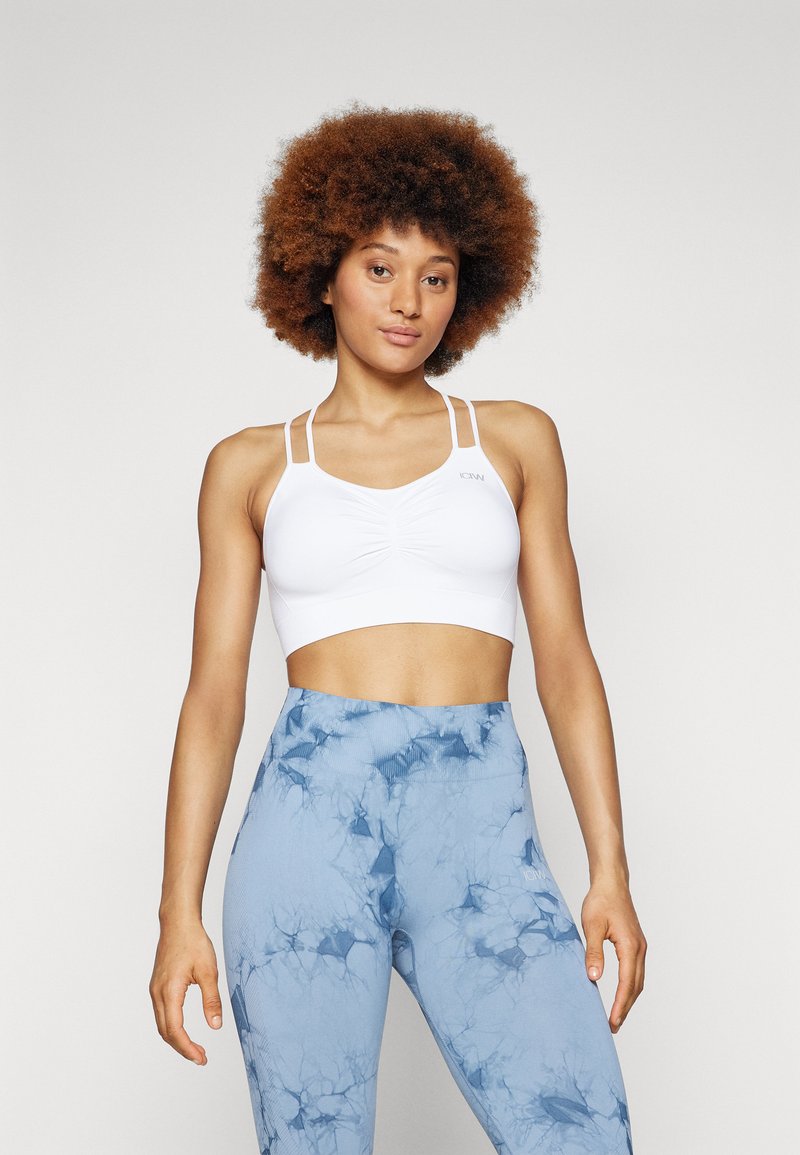 Soutien-gorge de sport blanc avec plusieurs fines bretelles et un détail froncé au centre, associé à un legging taille haute en marbré bleu avec une texture côtelée.