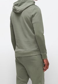 Felpa verde oliva con cappuccio regolabile, polsini e orlo a coste. Tessuto morbido, silhouette aderente e dettagli di cucitura minimal.
