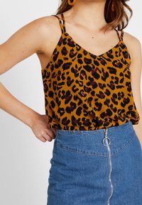 Top in stampa leopardata color senape con spalline sottili, abbinato a una gonna di jeans a vita alta con zip frontale e parti in metallo argentato.