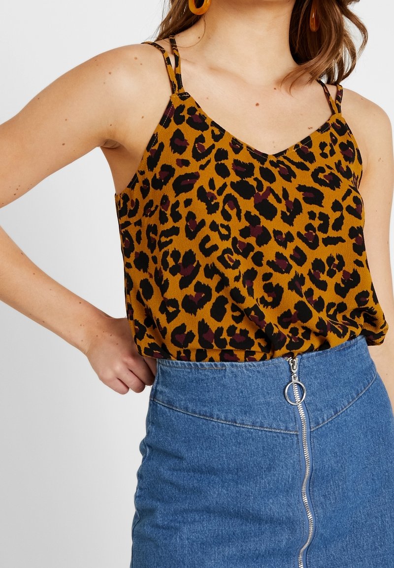 Top in stampa leopardata color senape con spalline sottili, abbinato a una gonna di jeans a vita alta con zip frontale e parti in metallo argentato.