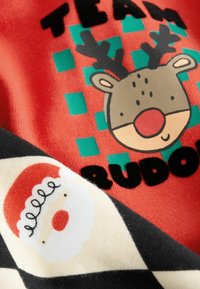 Roter Stoff mit einem Rentier-Motiv und dem Text "TEAM RUDOLPH"; daneben schwarzer und cremefarbener Stoff mit einem Santa-Gesicht-Muster; weiche Textur.