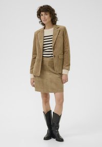 Blazer en velours côtelé marron et jupe assortie, associé à un pull rayé noir et blanc et des bottes de cowboy noires.
