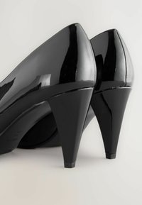 Tacones altos negros brillantes con punta afilada y tacón de aguja, que presentan una superficie suave y un diseño ligeramente curvado.