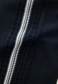 Tela de color azul marino con una superficie texturizada que presenta detalles de punto en blanco y una franja central decorativa. Con pequeños agujeros a lo largo de los bordes.
