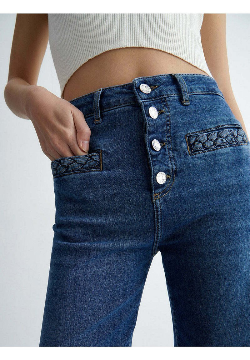 Jeans z wysokim stanem w ciemnoniebieskim kolorze z pięcioma guzikami, plecionymi akcentami kieszeni i gładką fakturą.