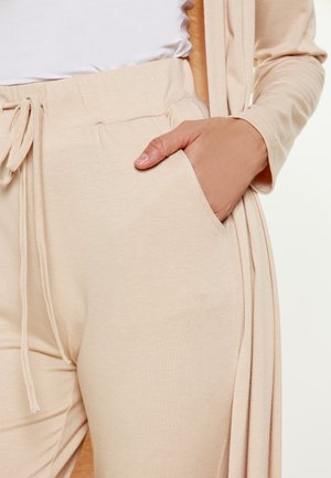 Beige loungewear setti, joka sisältää rento-leikkauksen yläosan ja naru-/kauttamahousut taskuilla. Suloinen tekstuuri, joka on kevyt ja hengittävä materiaali.