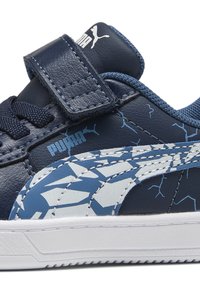 Baskets en cuir bleu marine avec des accents blancs et bleu clair à motifs, fermeture à lacets et Velcro, et semelle blanche texturée. Logo Puma sur le côté.