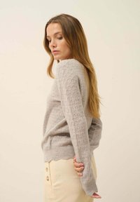 Un pull en tricot gris clair avec un motif en losanges, des manches longues, un ourlet en pointes, et une coupe décontractée, associé à un pantalon en velours côtelé beige.