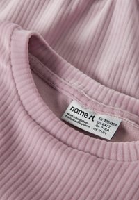 Nahaufnahme eines rosa gerippten Stoffkragens mit eingenähtem Etikett, das Kleidergrößen und den Text "Hergestellt in Bangladesch" zeigt.