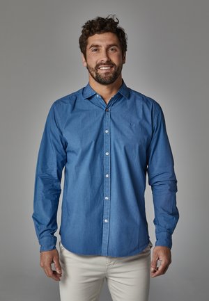 Camisa de botones de manga larga azul, hecha de una tela ligera, con un cuello tipo button-down, bolsillo frontal y un sutil detalle del logotipo.
