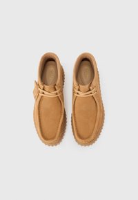 Tan leather shoes with a rounded toe, textured surface, tonal stitching, and rubber soles featuring a patterned tread. Two lace loops detail the upper.