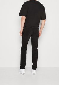 Camiseta negra de gran tamaño con mangas cortas combinada con jeans negros de corte recto. Zapatillas blancas en los pies. Diseño minimalista, sin patrones visibles.
