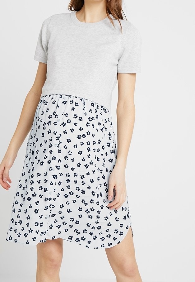 Haut gris à manches courtes avec un corsage ajusté au-dessus d'une robe bleu clair arrivant au genou, ornée d'un motif floral noir et d'un ourlet courbé.