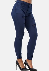 Jeans skinny azul marino con detalles desgastados, cintura alta y dobladillo deshilachado. Hechos de una tela elástica para mayor confort y ajuste.
