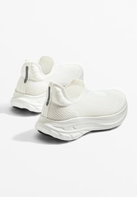 Biele slip-on tenisky s pletenou textúrou, s hladkou podrážkou a jemným zadným pútkom pre jednoduché obúvanie.