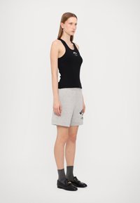 Melnas bezpiedurkņu tank top ar logotipu, pelēkas kokvilnas šortus ar teksta apdruku, pelēkas zeķes un melnas loafers, lai radītu ikdienišķu izskatu.