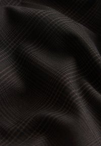 Tessuto a quadri scuro con motivo quadrettato rosso e nero sottile, mostrato con pieghe morbide e dettagli di texture.
