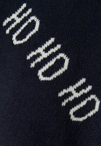 Tessuto a maglia blu navy con grande testo bianco decorato con un motivo ondulato. La texture è morbida e il design appare contemporaneo e pulito.