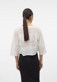 Witte gehaakte top met een losse pasvorm, brede mouwen, ingewikkelde patronen en een cropped ontwerp. Gecombineerd met een nauwsluitende zwarte rok.