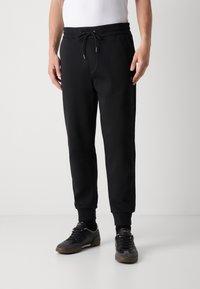 Svarta joggerbyxor med elastisk midja, justerbar dragsko, ribbade muddar och sidofickor. Mjukt tyg med en slät yta.