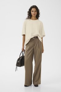 Beige oversized t-skjorte kombinert med høyt liv, vide brune bukser. Modellen holder en svart teksturert håndveske.