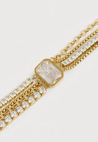 Χρυσό περιδέραιο πολλαπλής αλυσίδας με ένα μεγάλο ορθογώνιο διαφανές πολύτιμο λίθο στο κέντρο και σειρές από μικρότερους στρογγυλούς και τετράγωνους διαφανείς λίθους.